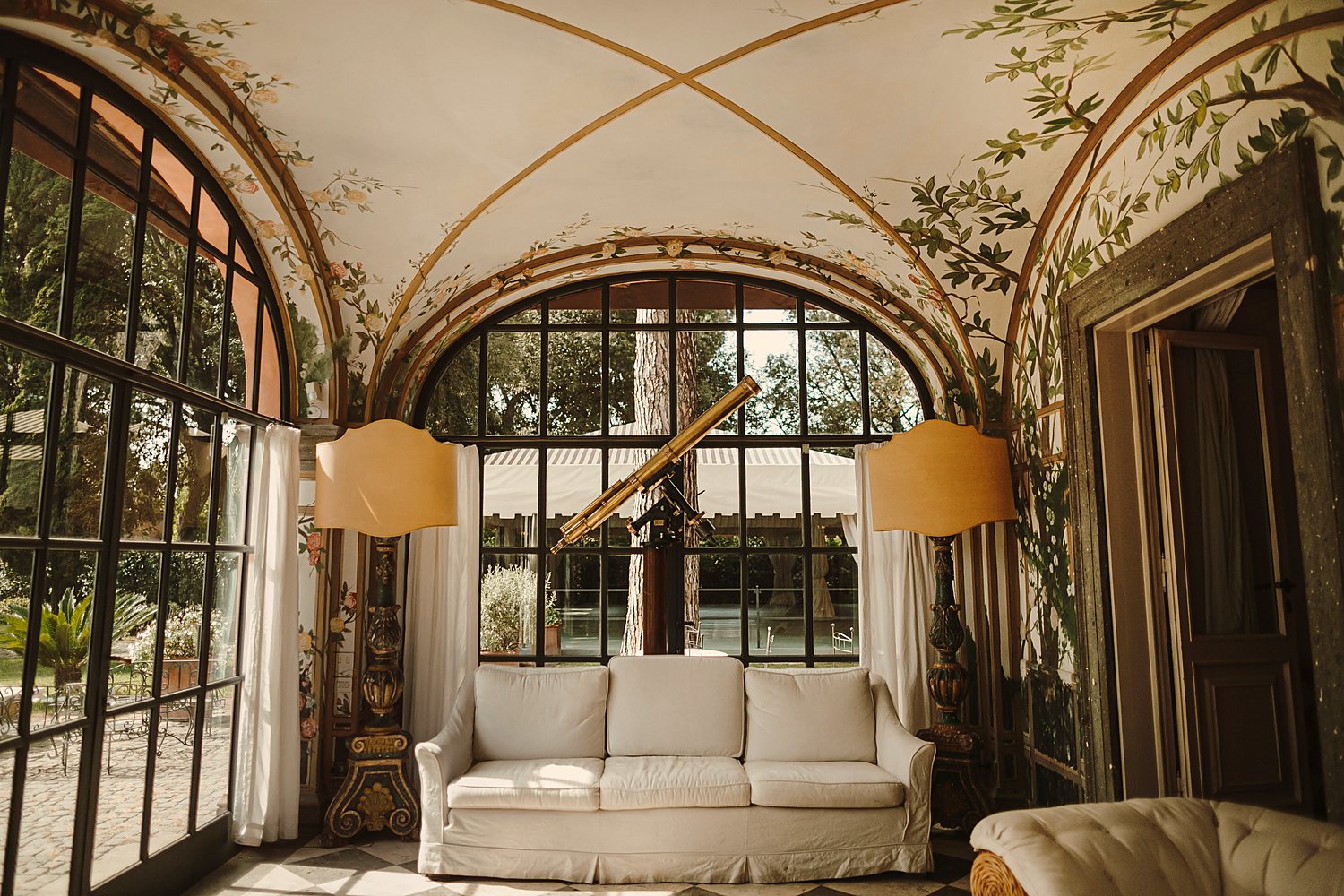 A frescoed garden room with arched windows and a brass telescope